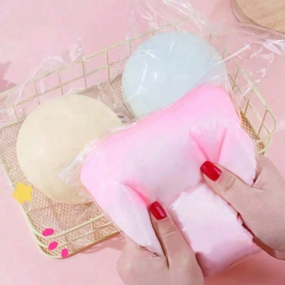Hände halten einen großen rosa Squishy-Ball und einen hellblauen Squishy in einer klaren Tasche auf einem geflochtenen Tablet