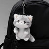 A soft grey cat plush charm attached to a black backpack zipper.