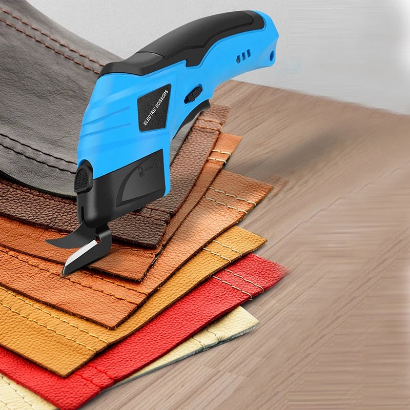 A blue cordless electric scissor tool is shown cutting fabric and leather materials on a wooden surface.