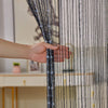 A hand is adjusting a sheer black and clear crystal beaded string curtain for a doorway or window.