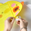 Hands are opening a yellow cartoon duck bath toy storage mesh bag with a suction cup on a white surface.