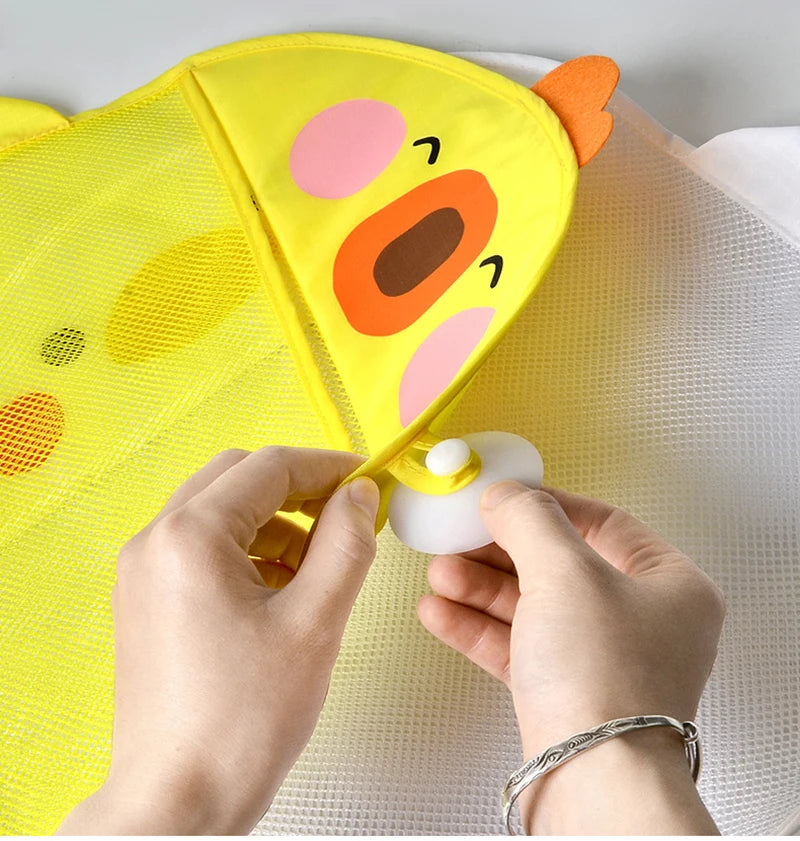 Hands are opening a yellow cartoon duck bath toy storage mesh bag with a suction cup on a white surface.