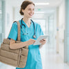 A nurse in blue scrubs holds a tablet and carries a beige quilted multi-compartment tote bag in a brightly lit hospital hallw