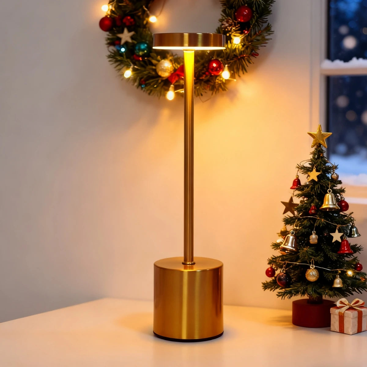 A gold-toned desk lamp with a brass finish and an illuminated shade, decorated with festive lights and greenery.