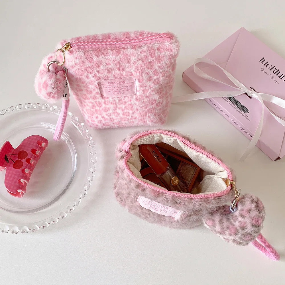 A pink leopard print cosmetic bag with a zipper and pink strap is shown next to a glass plate.