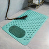 A teal non-slip bath mat with massage nodes and a suction cup is displayed on a light gray floor.