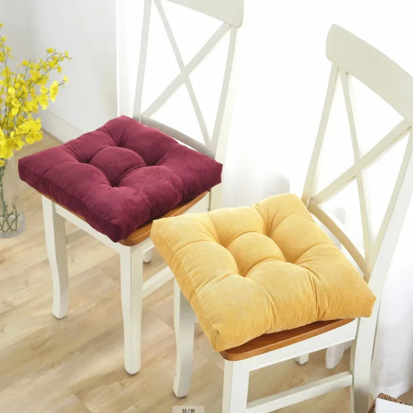 Two tufted floor seating cushions, one purple and one yellow, displayed on white wooden chairs.