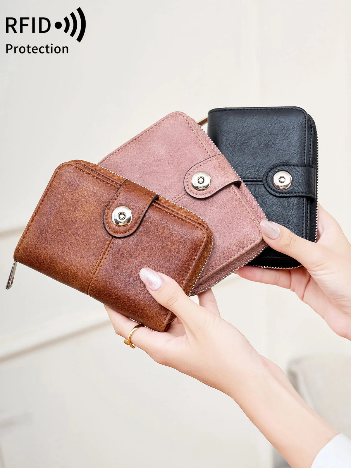 A hand holds a brown leather wallet and a black leather wallet, demonstrating RFID protection.
