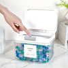 A hand opens an automatic pop-up laundry pod holder with an airtight lid revealing colorful laundry pods inside.