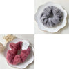 A pair of fluffy, gray plush coil hair ties resting on a white plate and a pink pair on another white plate.