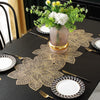 A set of ornate gold leaf floral PVC table runners and placemats displayed on a black table.