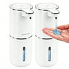 A white touchless automatic soap dispenser with a pump mechanism and a USB-C rechargeable battery is shown next to a hand.