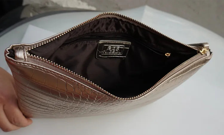 A close-up of a beige crocodile-embossed PU leather envelope clutch with a gold zipper and interior lining.