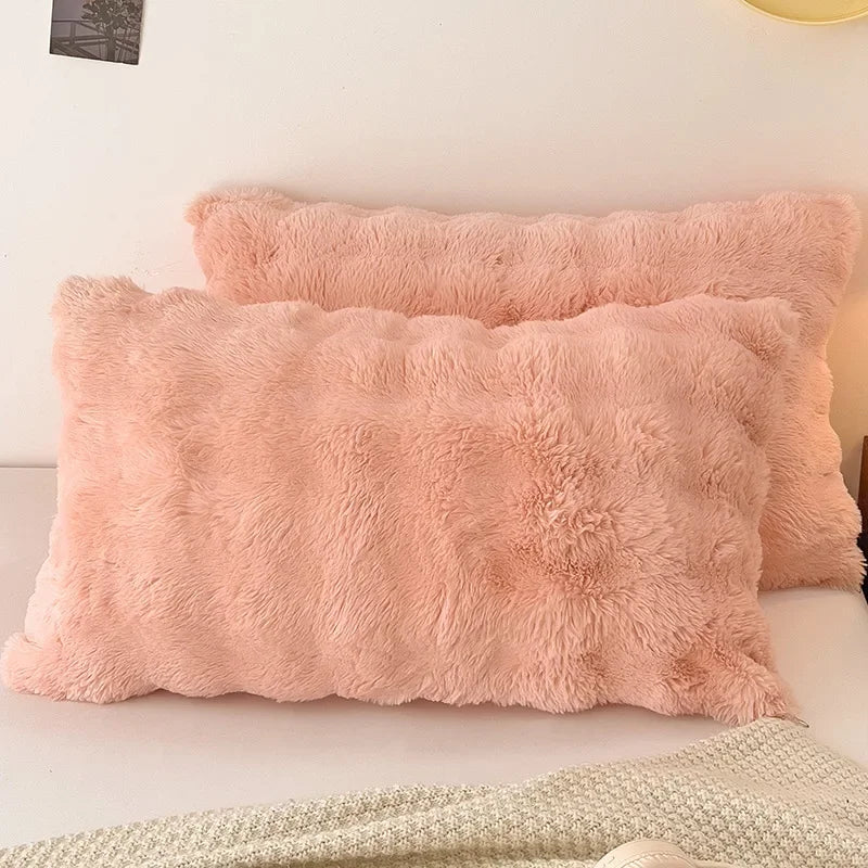 A fluffy, light pink quilted velvet pillow is displayed on a white surface.
