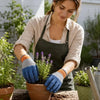 A woman wearing blue gardening gloves is planting a plant in a terracotta pot outdoors.