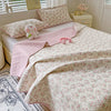 A pink floral quilted bedspread with a matching pink coverlet and pillows on a bed.