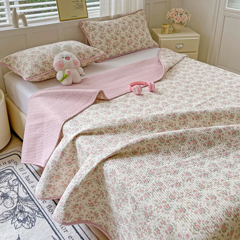 A pink floral quilted bedspread with a matching pink coverlet and pillows on a bed.