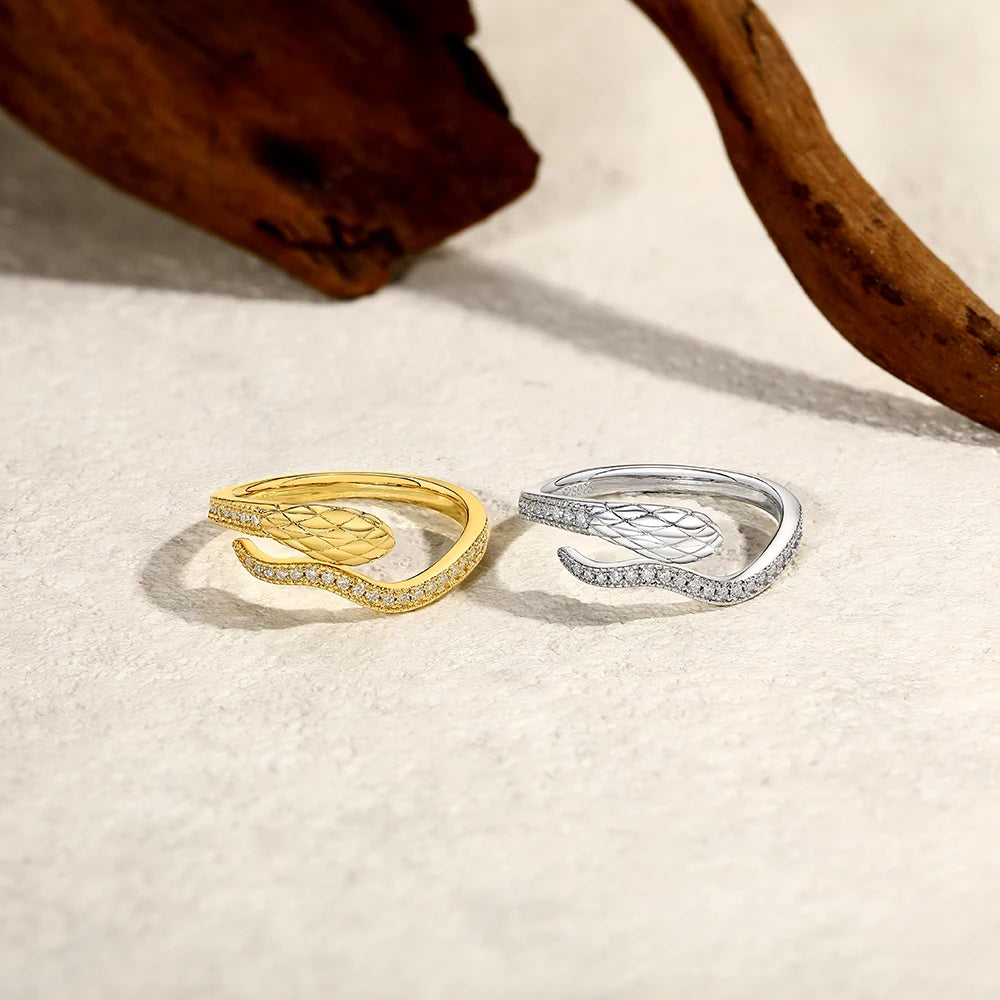 A pair of snake-design moissanite rings, one gold-toned and one silver, resting on a light surface.