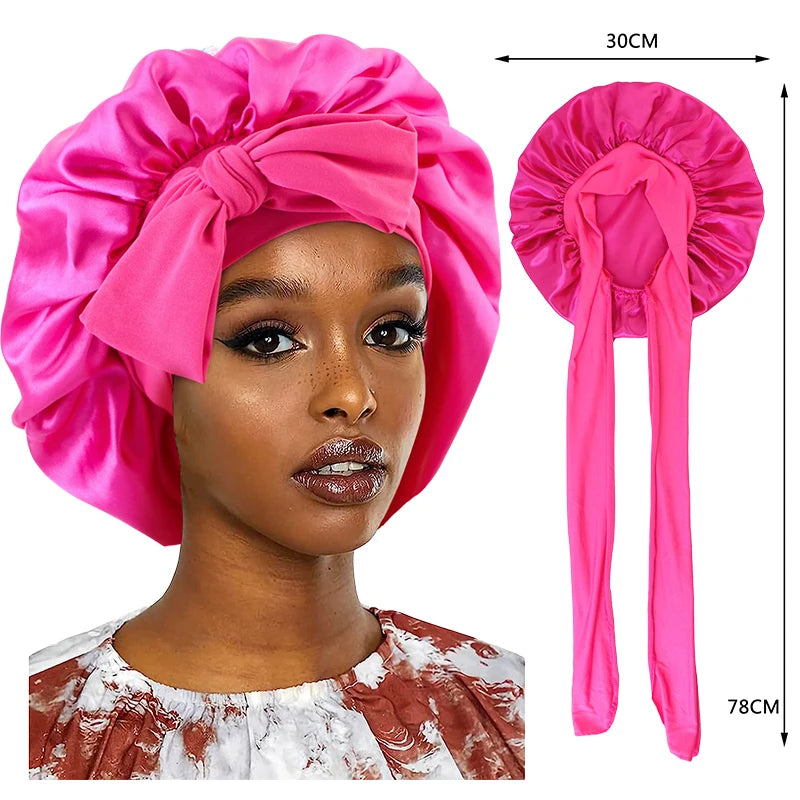 A pink silky satin sleep cap with a wide band shown on a model's head and a separate product view.