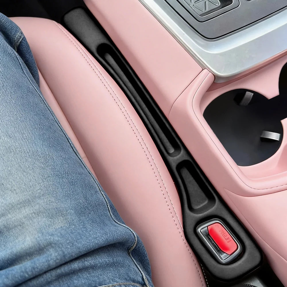 A close-up view of a pink car seat gap filler and organizer with a black handle and red button.