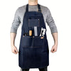 A dark blue denim work apron with multiple pockets and a leather strap is worn over a gray long-sleeved shirt.