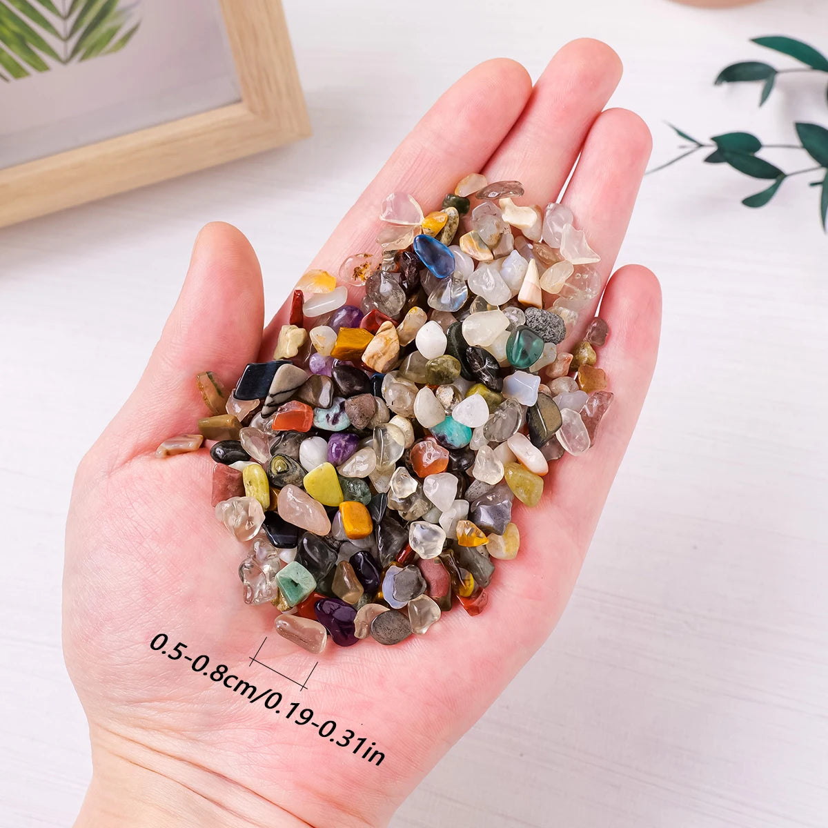 A hand holds a pile of mixed natural crystal gravel stones and gemstone chips for home decor