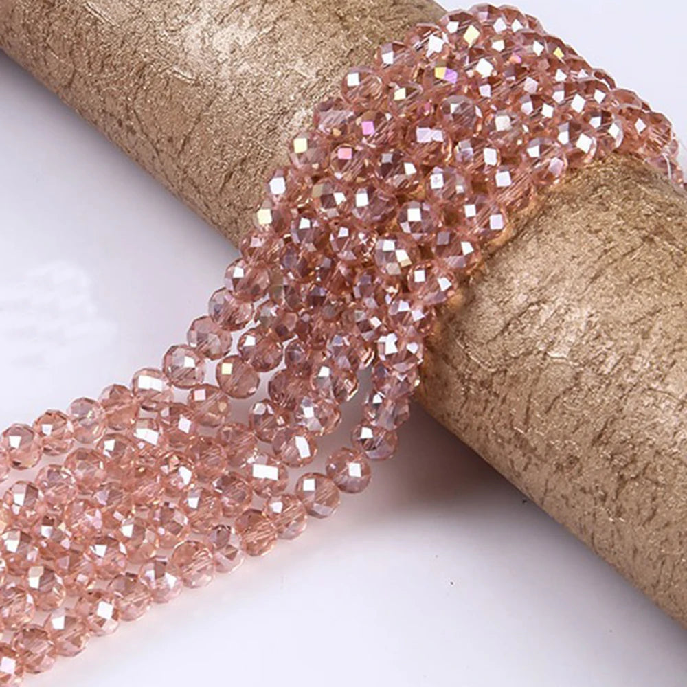 A strand of rose gold faceted crystal glass spacer beads is unwrapped on a beige cylindrical object.