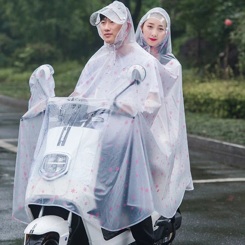 Two people wearing transparent waterproof motorcycle rain ponchos with hoods standing next to a white motorcycle.