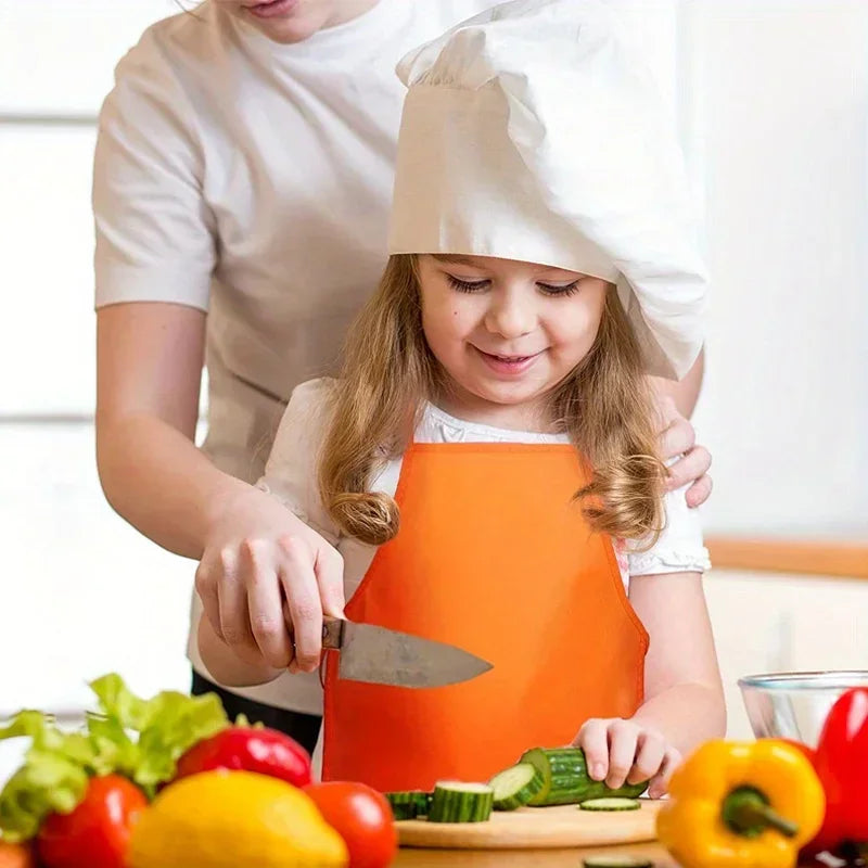 A young girl is wearing an orange fabric apron while being assisted by an adult, with fresh produce on a wooden cutting board