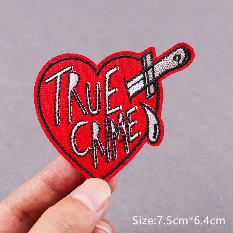 Red heart shaped embroidered patch with the text True Crime and a crossed knife design
