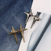 Two gold-toned Y2K star waist tightener clips for jeans resting on a white surface.