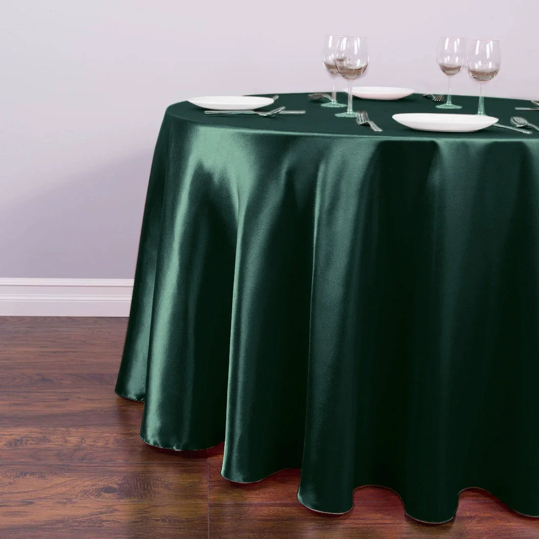 A dark emerald green satin tablecloth set for an event with white plates and silverware.
