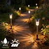 A row of modern solar powered garden lantern lights lining a dirt path in a garden setting.