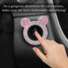 A hand presses a pink glittery bear-shaped ignition button on a car interior panel.