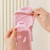 A hand is holding a pink foldable EVA travel slipper, showing the texture and design of the product.