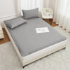 A gray waterproof mattress protector is displayed on a bed, featuring a quilted texture and white elastic straps.