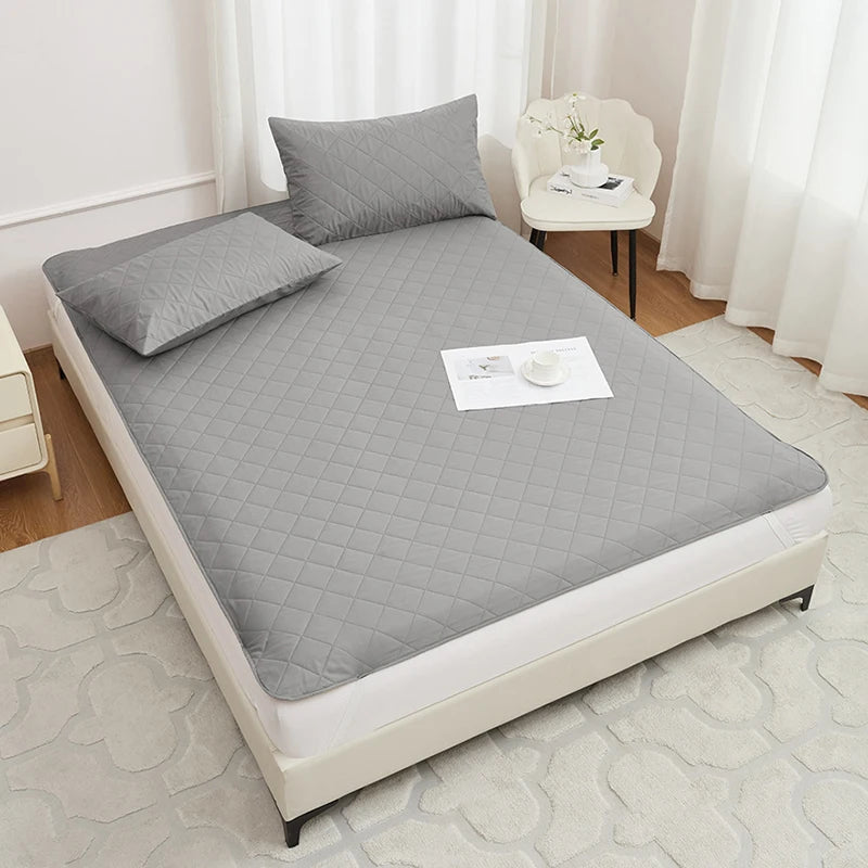 A gray waterproof mattress protector is displayed on a bed, featuring a quilted texture and white elastic straps.