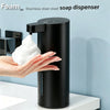A hand is dispensing white foam soap from a black stainless steel touchless automatic soap dispenser.