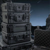 A stack of dark gray hard shell protective storage cases for tools and instruments resting on a rocky surface.