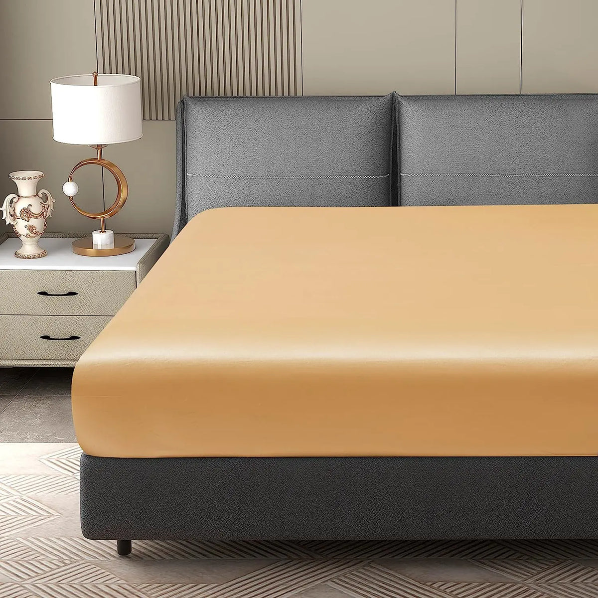A luxury satin fitted sheet is displayed on a bed with gray bedding and a bedside table.