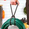 A hand is holding a heavy-duty hook and loop storage strap with a black handle, positioned over a green coiled cable.