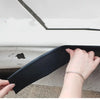 A hand is holding a black self-adhesive car door edge protector strip against a white surface.