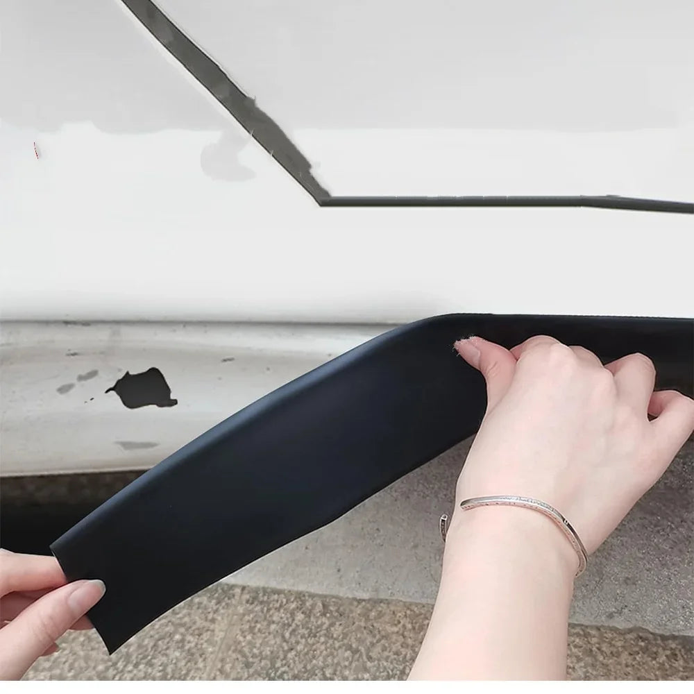 A hand is holding a black self-adhesive car door edge protector strip against a white surface.