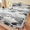 A gray and white faux fur fitted sheet is draped over a bed, with a small bottle resting on the fabric.