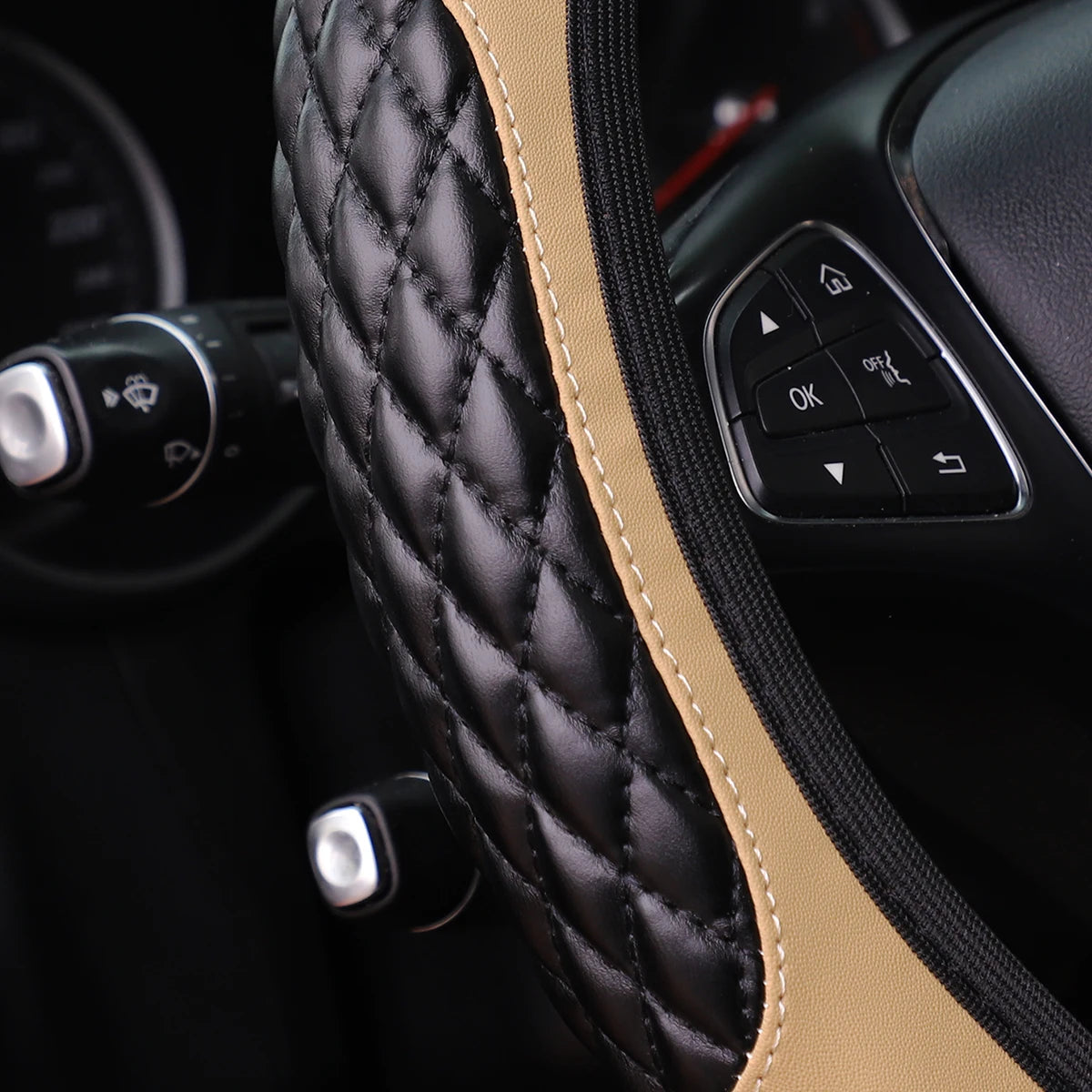 Close-up of a black quilted steering wheel cover with tan stitching and controls on the side.