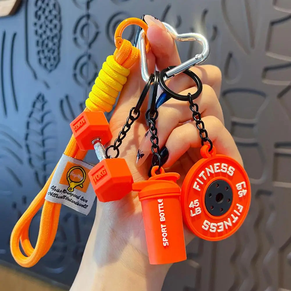 A hand holds an orange and black fitness keychain featuring a gym-inspired weight and a fitness disk.