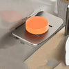 An orange wall-mounted aluminum soap dish with a drain is shown mounted on a gray surface.