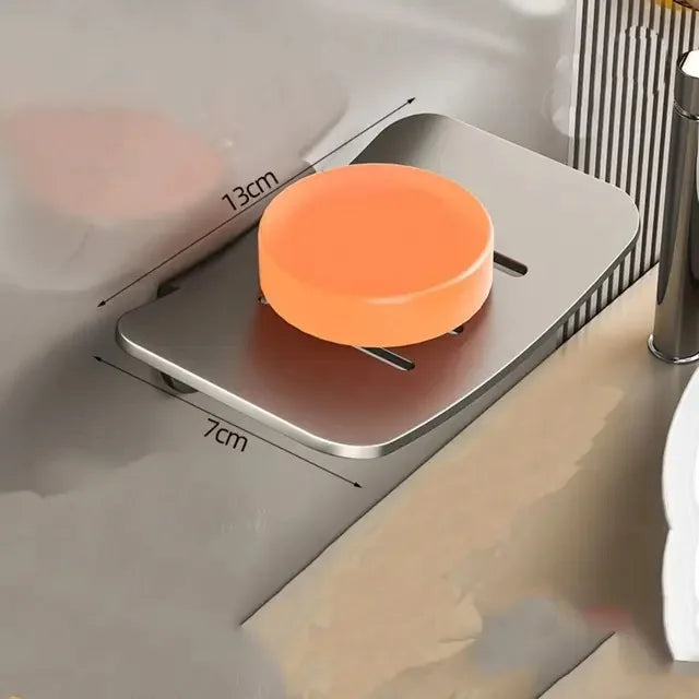 An orange wall-mounted aluminum soap dish with a drain is shown mounted on a gray surface.
