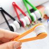 A hand holds an orange portable double-sided glasses cleaning brush with a white microfiber pad.