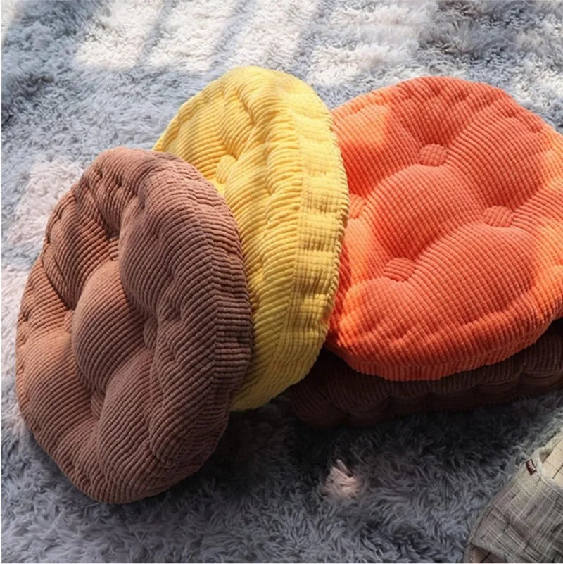 Three thick corduroy floor cushions in shades of yellow, orange, and brown resting on a gray fuzzy surface.